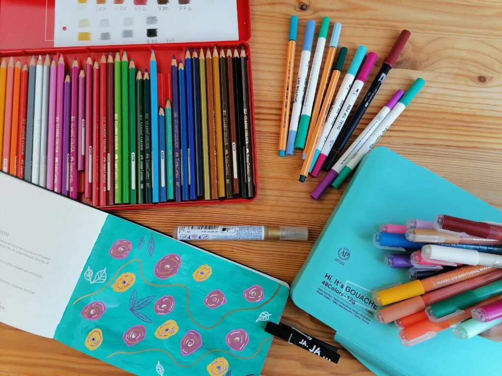 Bunte Stifte, ein Sketchbock liegen ausgebreitet auf einem Tisch